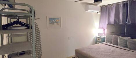 A bedroom with a bed, a ceiling fan, a wall-mounted heater, and a metal shelf unit.
