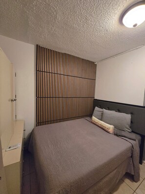 A bedroom with a bed, a headboard, a wall panel, and a door.