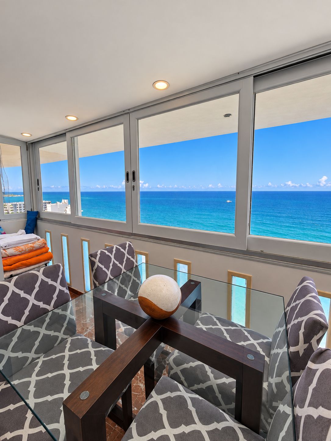 A modern room with a glass table, patterned sofas, and a view of the ocean.