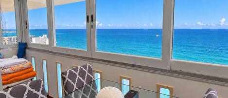 A modern room with a glass table, patterned sofas, and a view of the ocean.