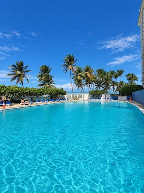 A clear blue pool with lounge chairs and palm trees.