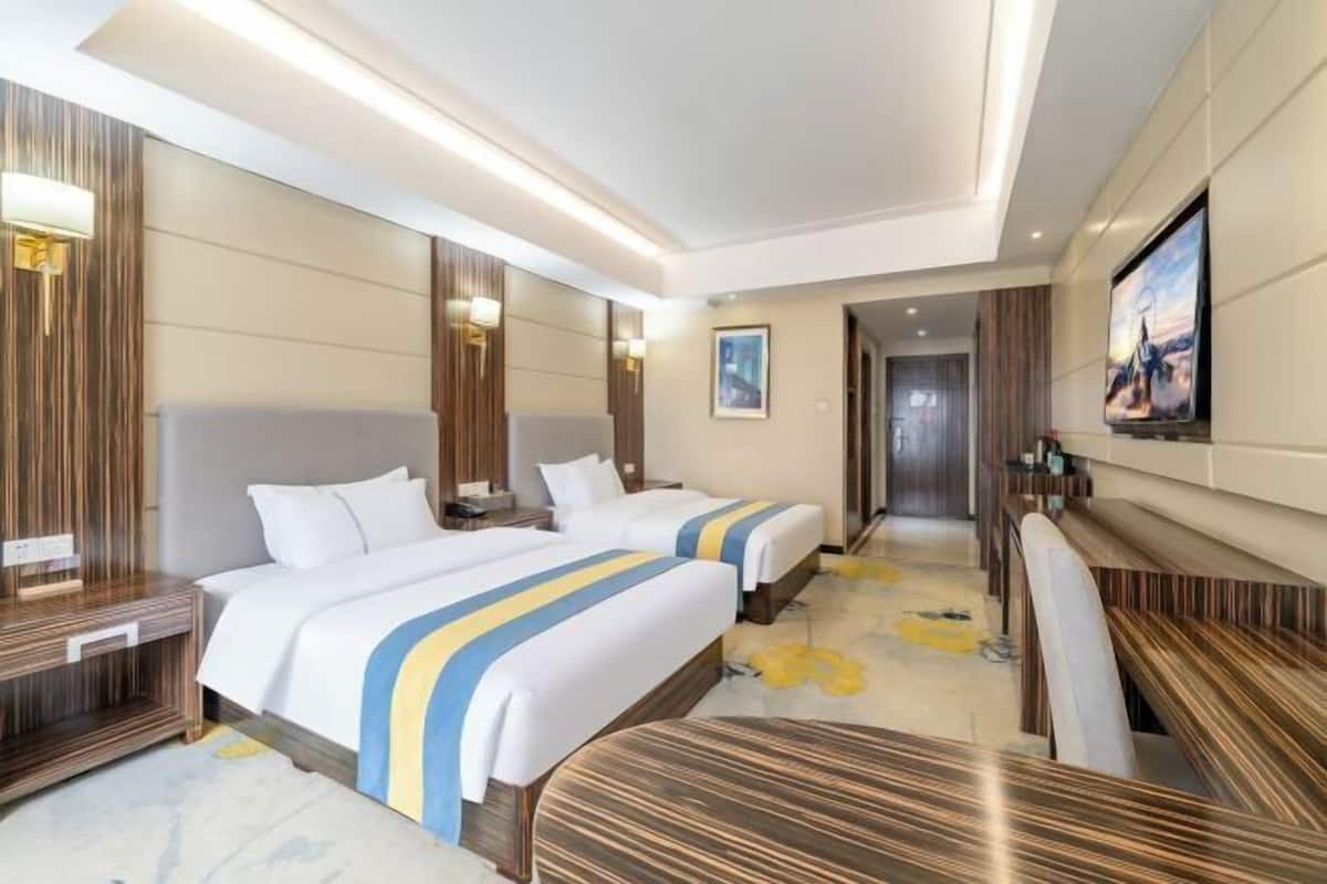 Une chambre d’hôtel avec deux lits, une télévision, un bureau et une salle de bain visible à travers une porte ouverte.