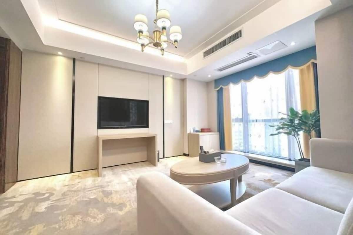 Une chambre d’hôtel moderne équipée d’un téléviseur à écran plat, d’une table basse ronde, d’un canapé et d’une grande fenêtre avec des rideaux.