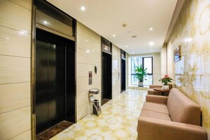 A hotel lobby with elevators, a reception desk, and a sofa.