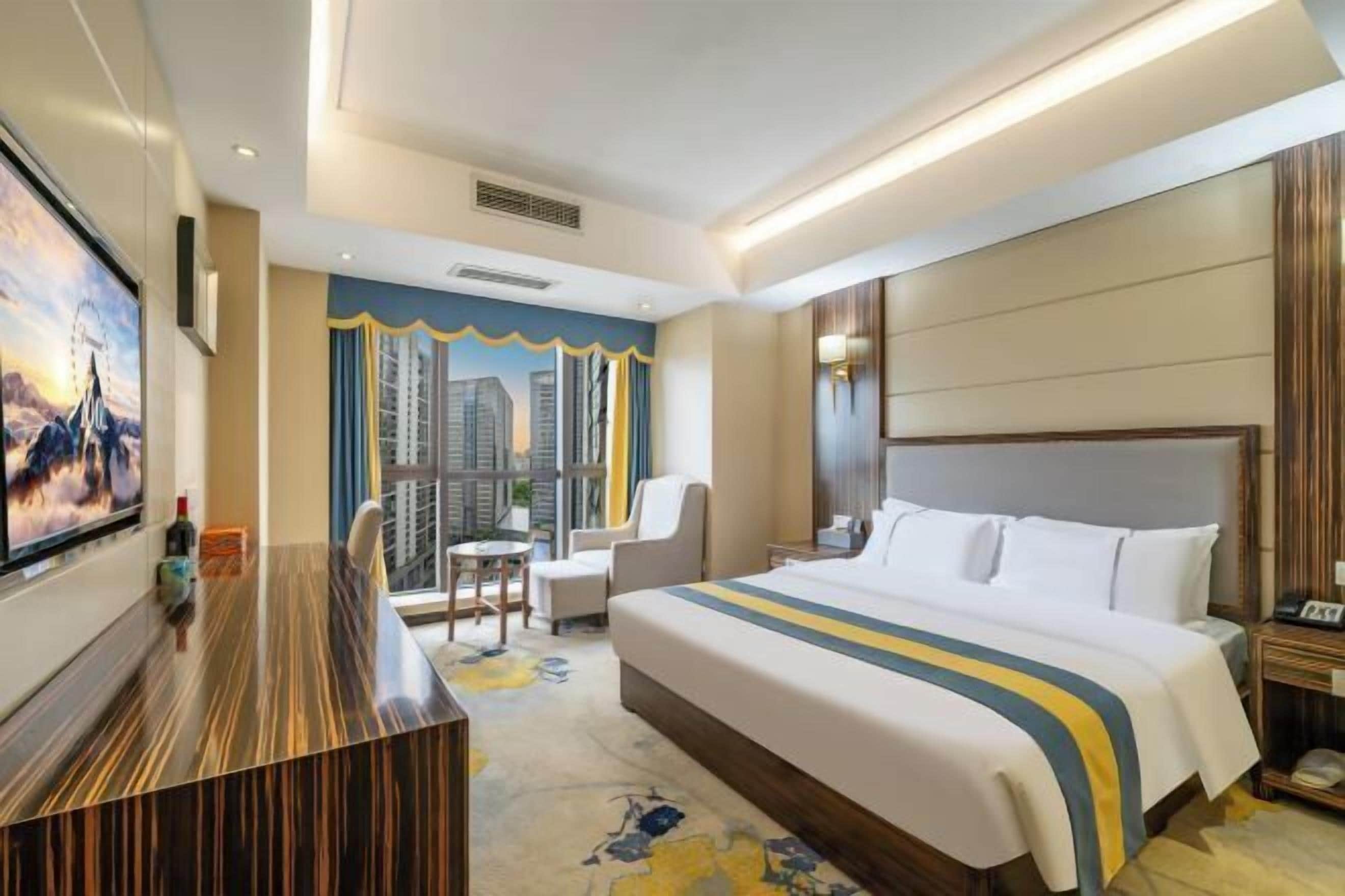 Quarto de hotel com uma cama grande, uma escrivaninha, uma cadeira, uma mesinha e uma televisão.