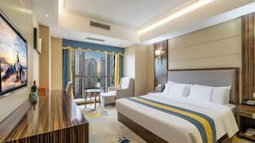 Quarto de hotel com uma cama grande, uma escrivaninha, uma cadeira, uma mesinha e uma televisão.