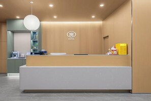A hotel reception area with a reception desk, a wall-mounted logo, and a counter with a yellow sign.