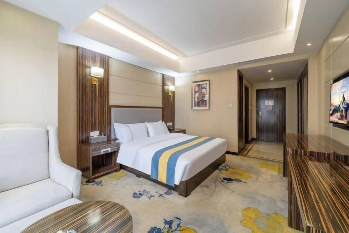 Une chambre d’hôtel avec un lit, un canapé, une télévision, un bureau et une salle de bain, le tout visible à travers une porte ouverte.