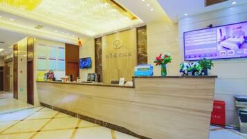 A hotel reception area with a reception desk, a digital screen, and a wall-mounted television.