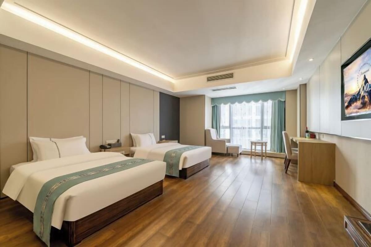 A hotel room with two beds, a desk, a chair, and a large window.