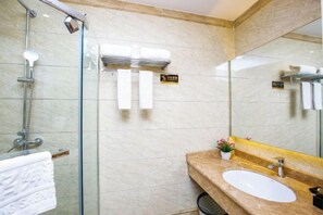 Uma casa de banho moderna com cabine de chuveiro em vidro, parede revestida a mármore, lavatório com espelho e porta-toalhas.