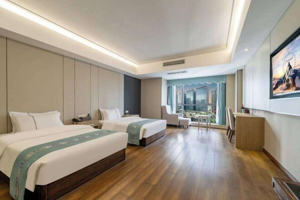 Une chambre d’hôtel avec deux lits, un bureau, une chaise, une table à manger et une grande fenêtre.