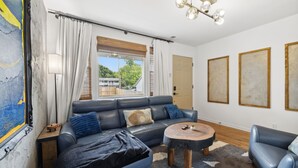 A modern living room with a blue sofa, a round coffee table, and a large window with curtains. - Escape to Nashville: 15 min to Downtown & BNA, sleeps 4, gated parking! (Madison)