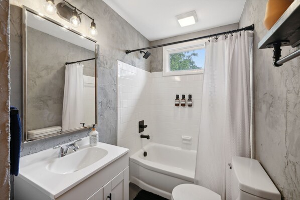 A bathroom with a white sink, a bathtub, a toilet, and a window with a shower curtain.