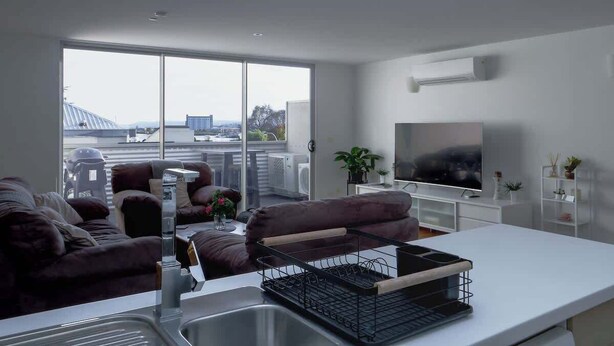 Un soggiorno moderno con divano, televisore, angolo cottura con lavello e balcone con vista.