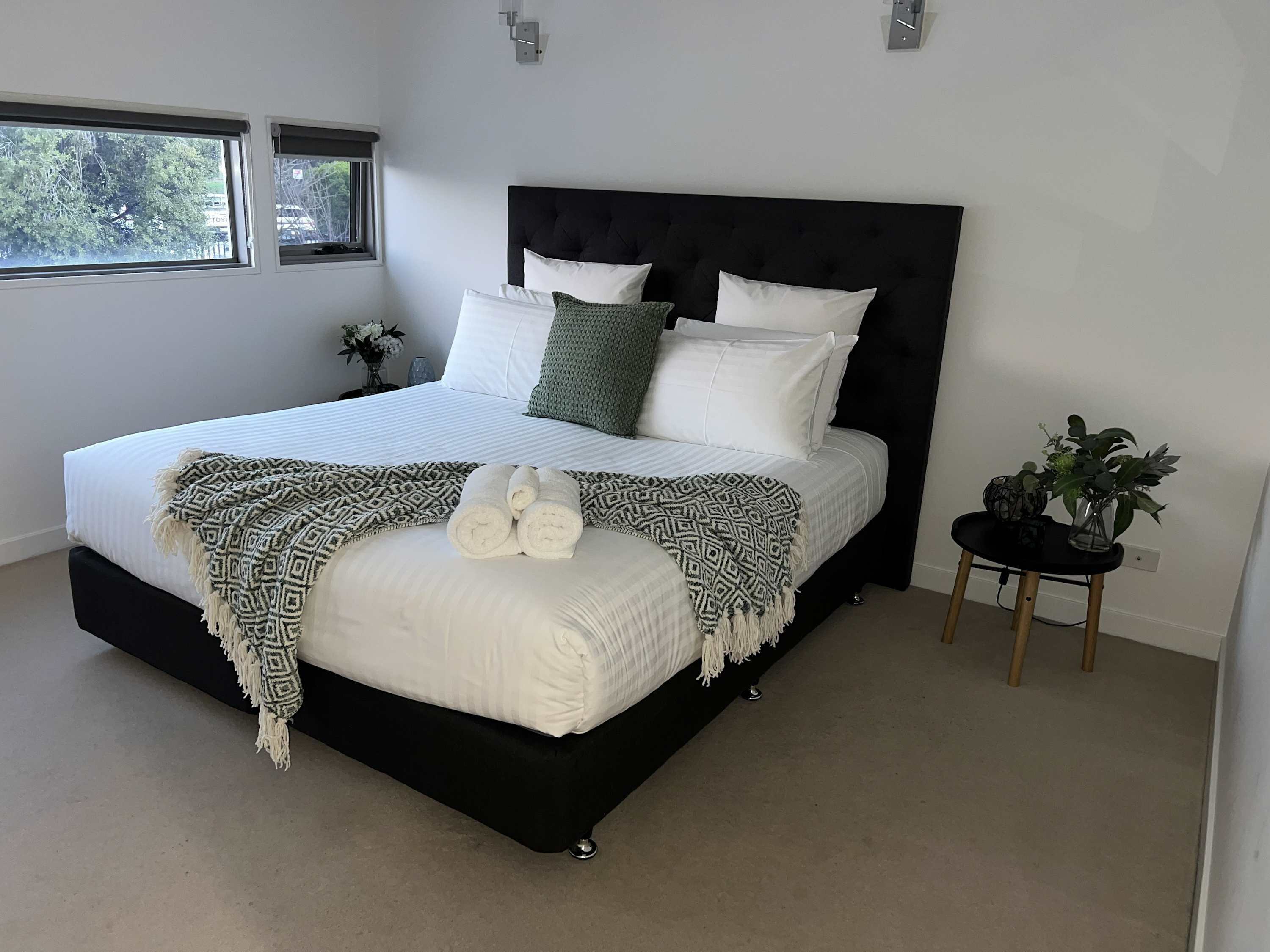 A modern bedroom with a large bed, a black headboard, and a small side table with a plant.