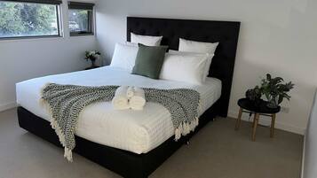 A modern bedroom with a large bed, a black headboard, and a small side table with a plant.