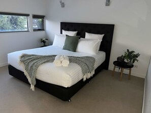 Une chambre à coucher moderne avec un grand lit, une tête de lit noire et une petite table de chevet agrémentée d’une plante.