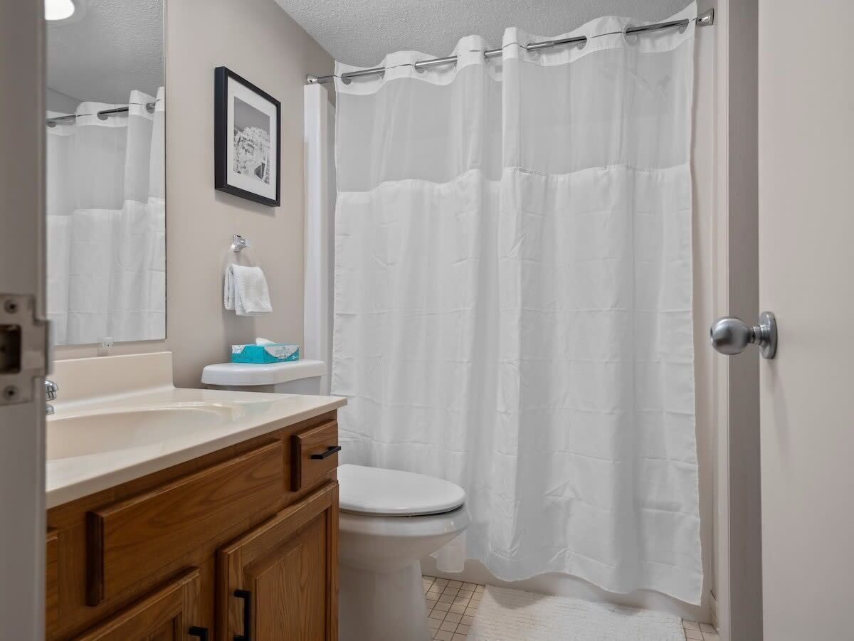 Un baño con lavamanos blanco, tocador de madera, inodoro y cortina de ducha.