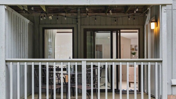 A wooden porch with a white railing, a table with chairs, and a door leading to an interior space. - GT Resort Area I Fireplace + Golf Views (Williamsburg)