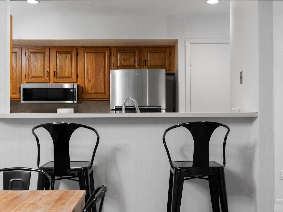 Una cocina moderna con gabinetes de madera, electrodomésticos de acero inoxidable y sillas negras.