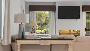 A hotel room with a bed, a desk with a lamp, a TV, and a view of greenery outside. - GT Resort Area I Fireplace + Golf Views (Williamsburg)