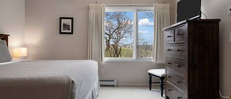 A bedroom with a bed, a dresser, a chair, and a window with curtains.