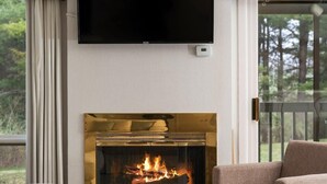 A living room with a fireplace, a television mounted on the wall, and a view of the outdoors through a window. - GT Resort Area I Fireplace + Golf Views (Williamsburg)