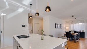 A modern kitchen with a central island, pendant lighting, and a dining area with a wooden table and chairs. - StayAU Newly Cozy Holiday House Tarneit (Tarneit)