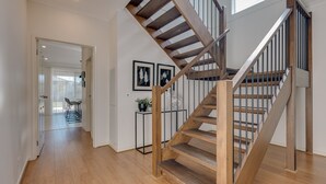 A wooden staircase with a metal railing, leading to an upper floor. A small table with a plant is visible on the landing. - StayAU Newly Cozy Holiday House Tarneit (Tarneit)