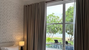 Un dormitorio con cama, mesita de noche, lámpara, ventilador de techo y vista a una piscina exterior y a la playa.