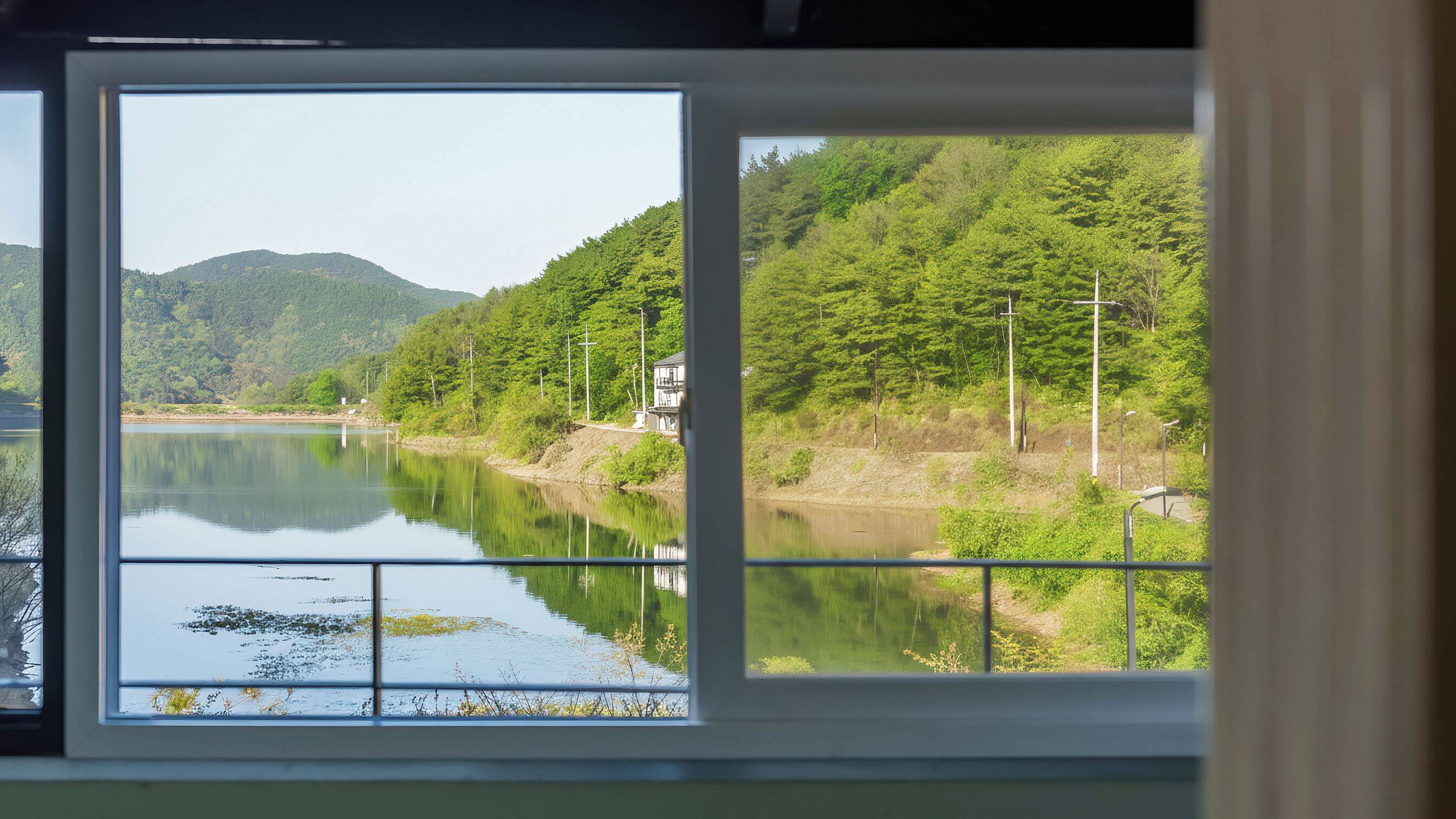 Vista desde una ventana de un río tranquilo, rodeado de exuberante vegetación y colinas.