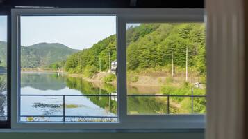 Une vue à travers une fenêtre sur une rivière paisible, bordée d’une végétation luxuriante et entourée de collines.