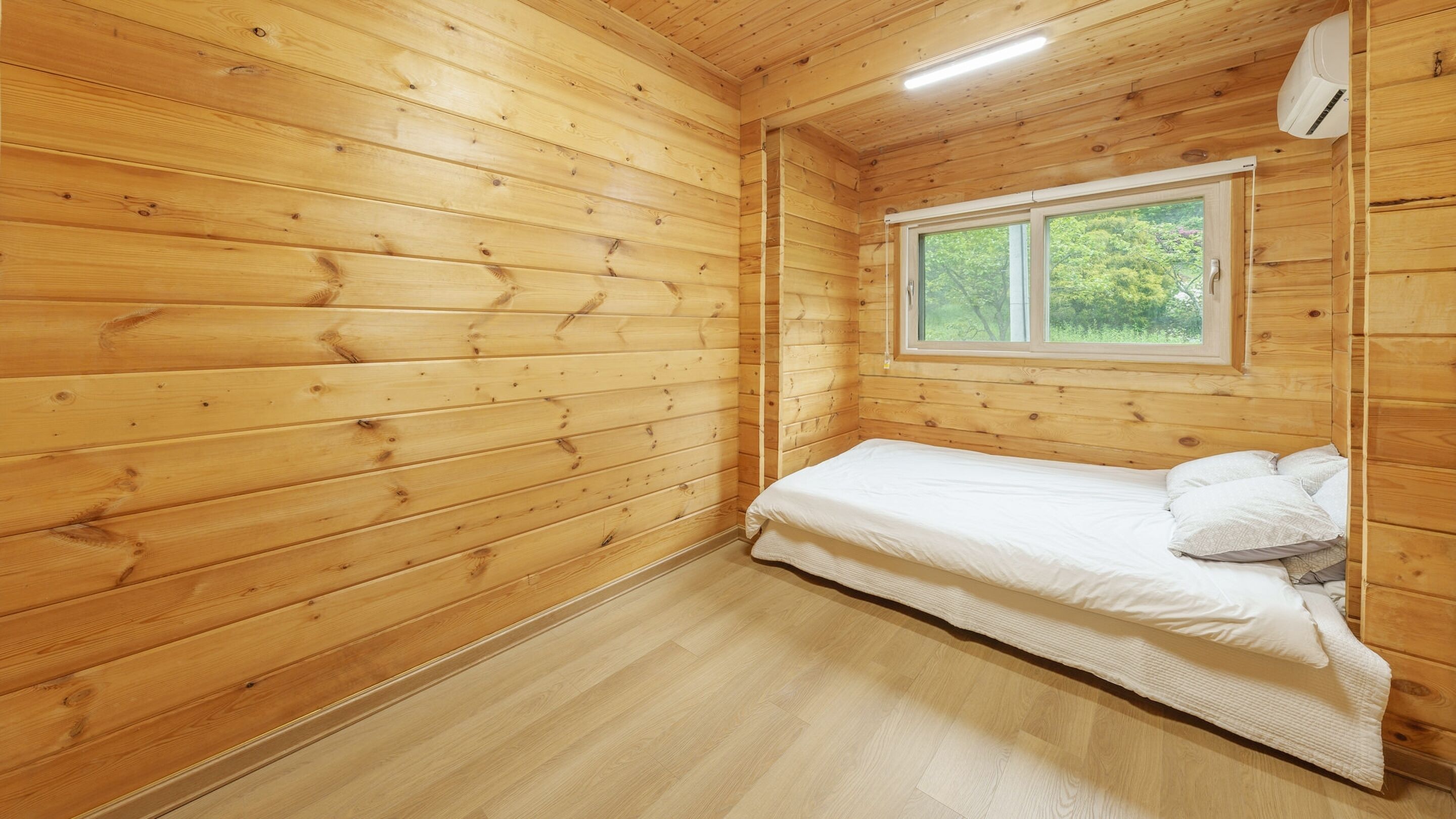 Ein Zimmer in einer Holzhütte mit einem Einzelbett, einem Fenster und einer Deckenleuchte.
