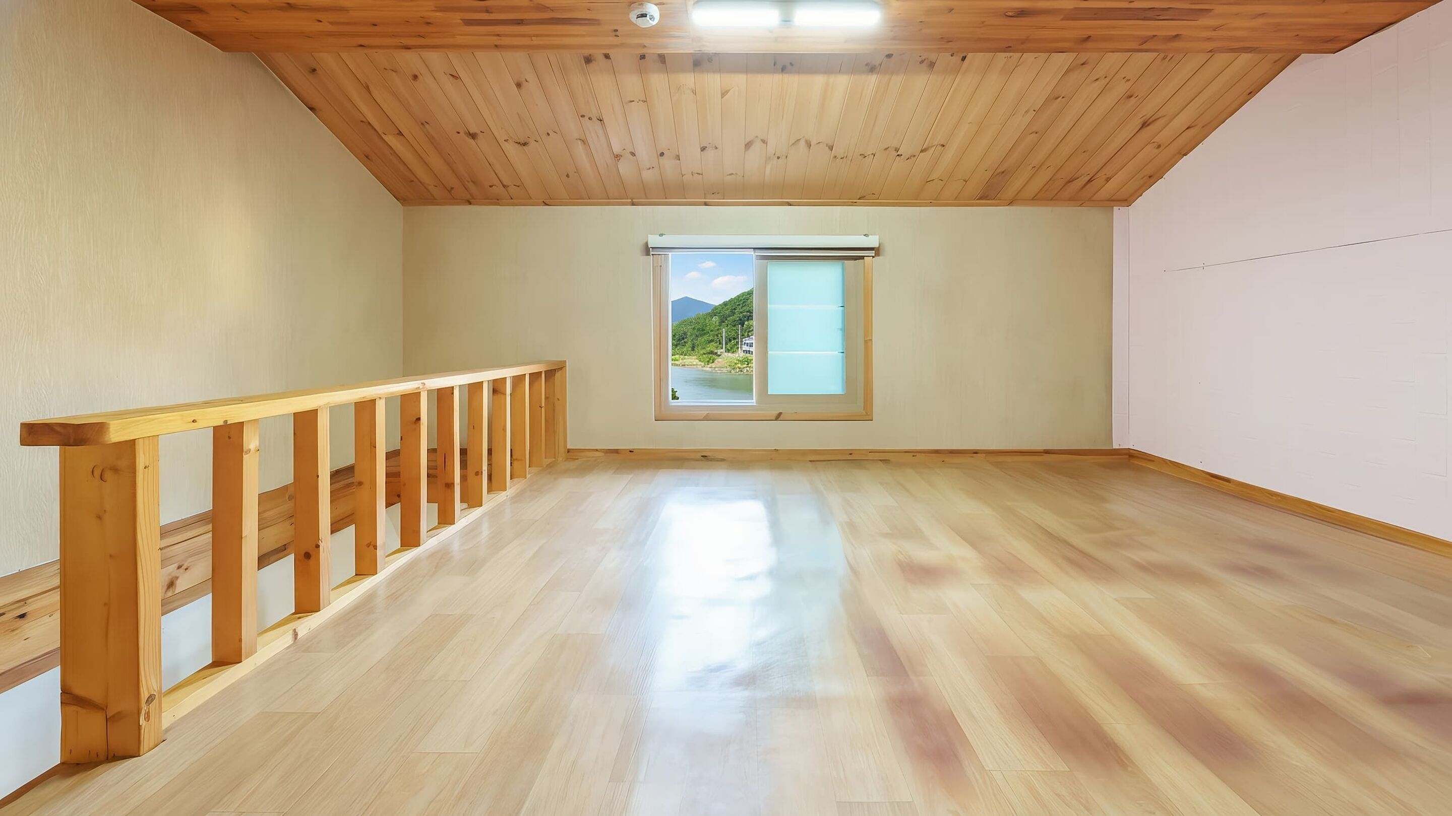 Habitación amplia con suelo y barandilla de madera, y un ventanal con vistas a zonas verdes y montañas.