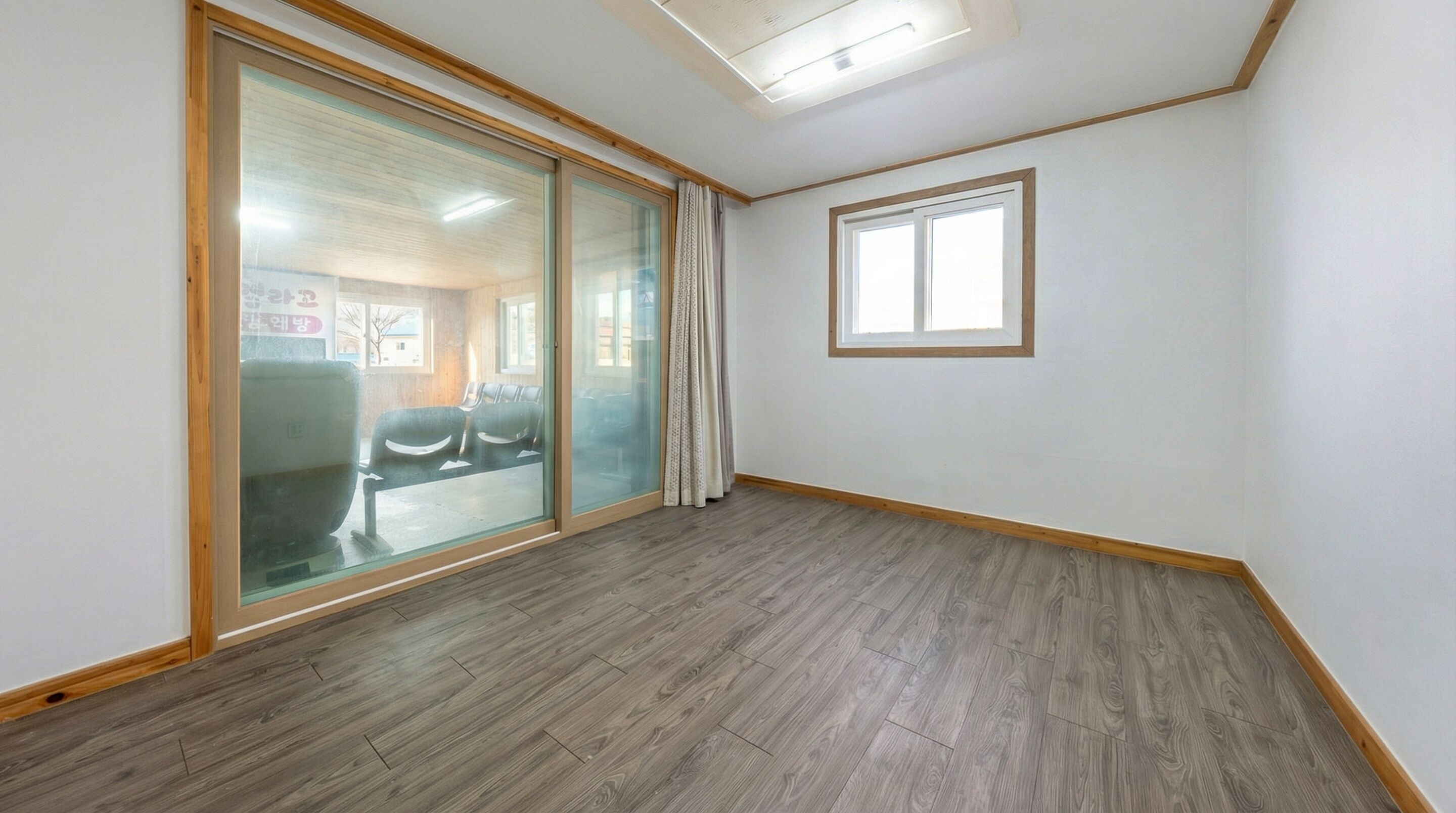 A room with a large sliding glass door leading to an outdoor area, a small window, and wooden flooring.