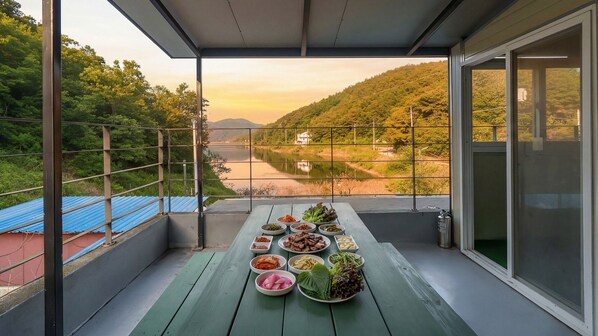 A balcony with a table set for a meal, overlooking a river and hills.