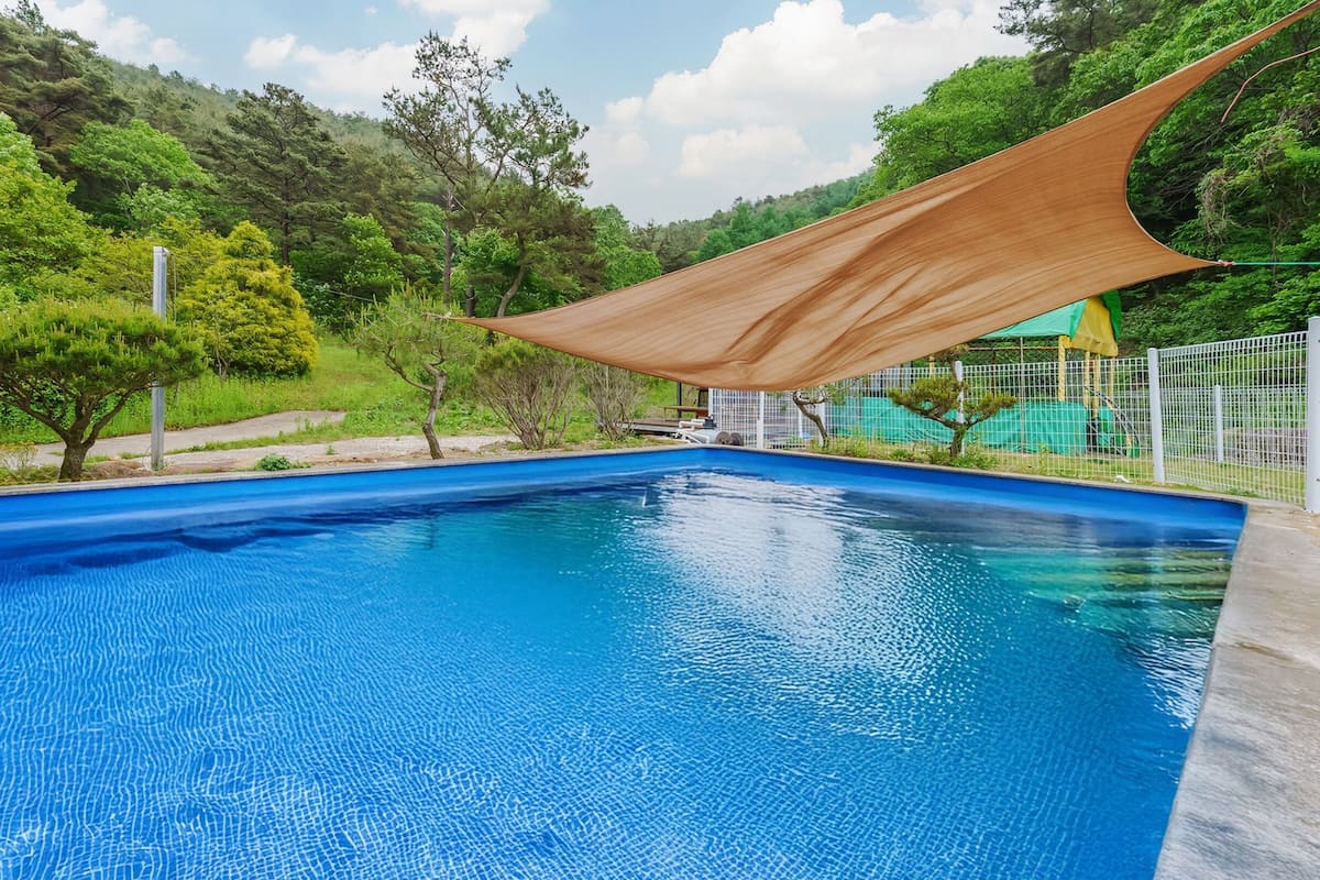 A rectangular swimming pool with clear blue water, surrounded by a wooden deck and a white fence.