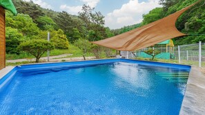 Una piscina rectangular con agua cristalina azul, rodeada por una terraza de madera y una cerca blanca.