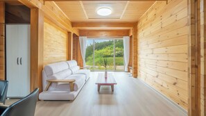 Un interior de madera con un sofá, una mesita y vistas al exterior con vegetación.