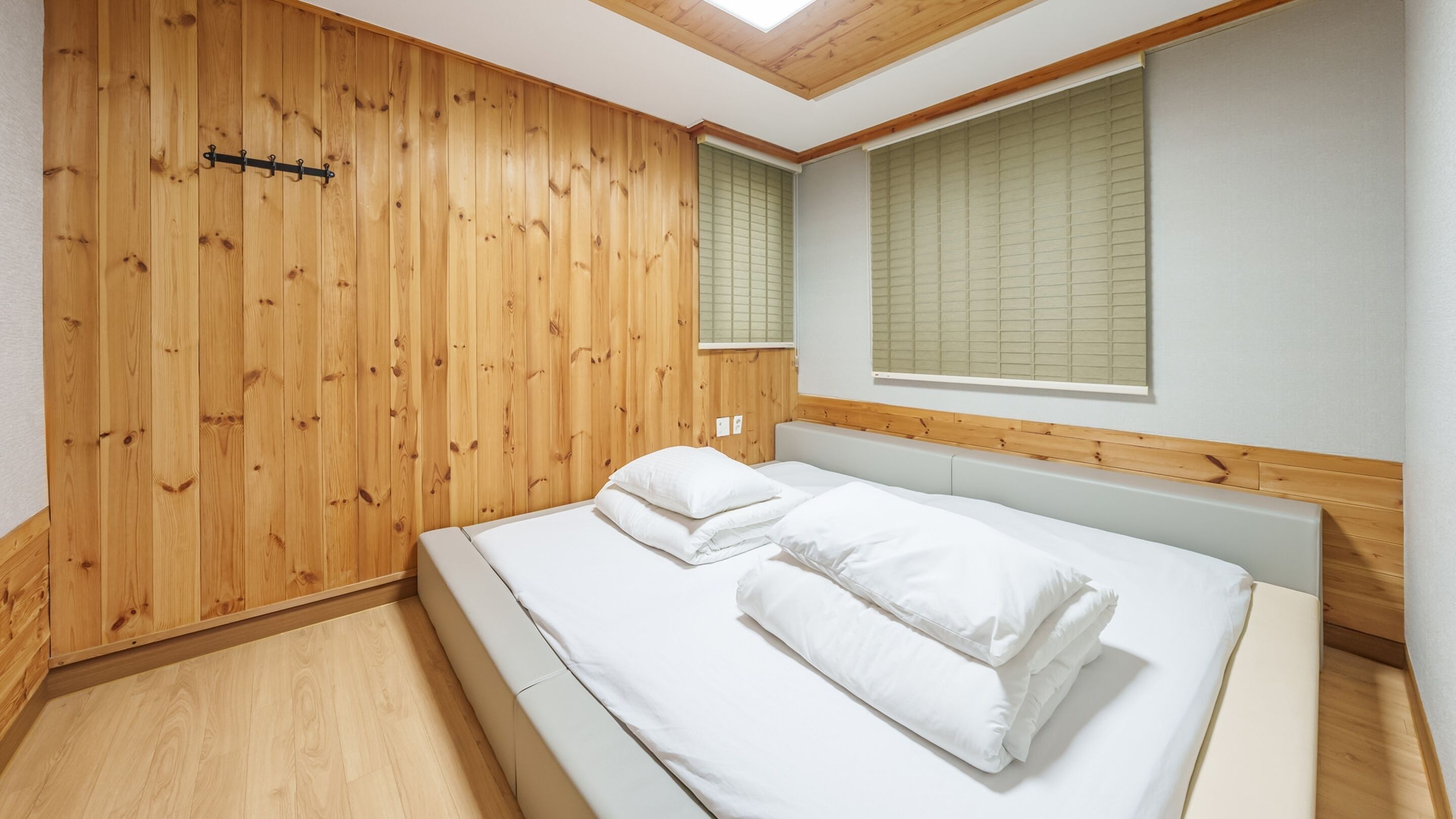 Ein Schlafzimmer mit einer Holzwand, einem Bett mit weißer Bettwäsche und einem Oberlicht.
