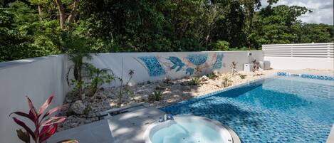 A swimming pool with a mosaic tile design, a hot tub, and a wall with a decorative mural.