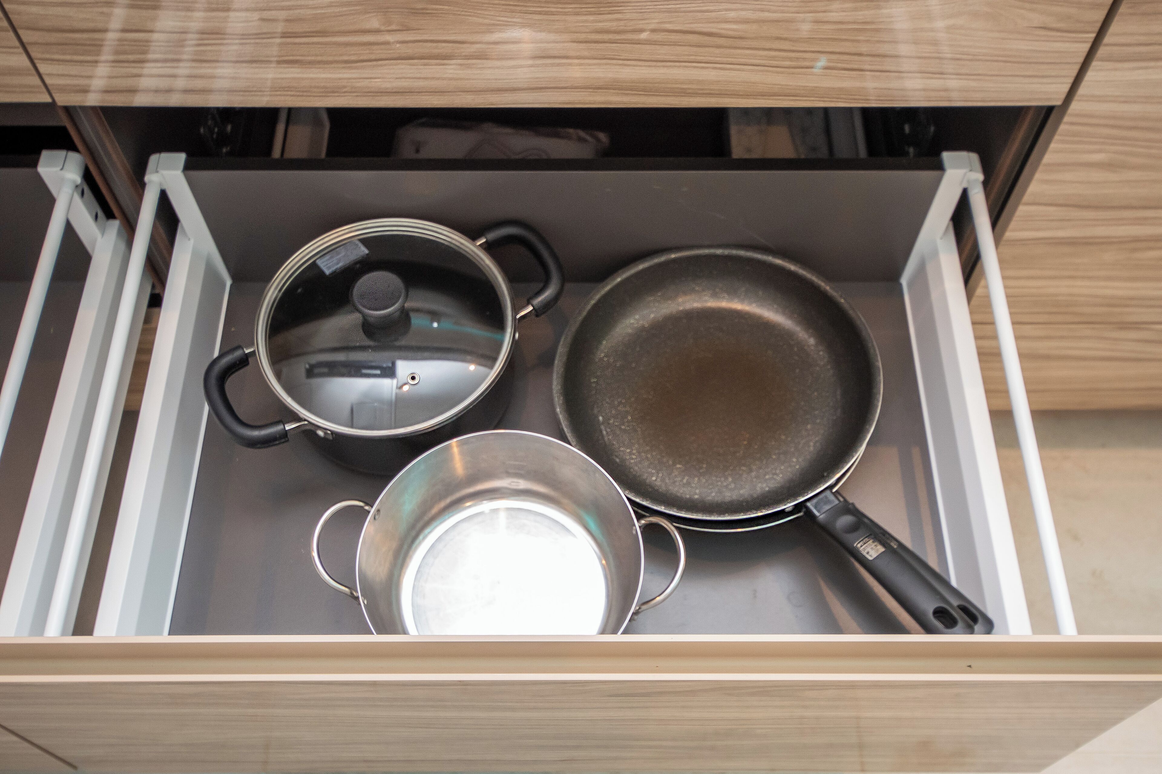 A kitchen drawer containing a frying pan, a pot with a lid, and a saucepan.