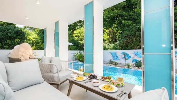 Un área de comedor exterior moderna con vista a la piscina, mobiliario blanco y cielo despejado.