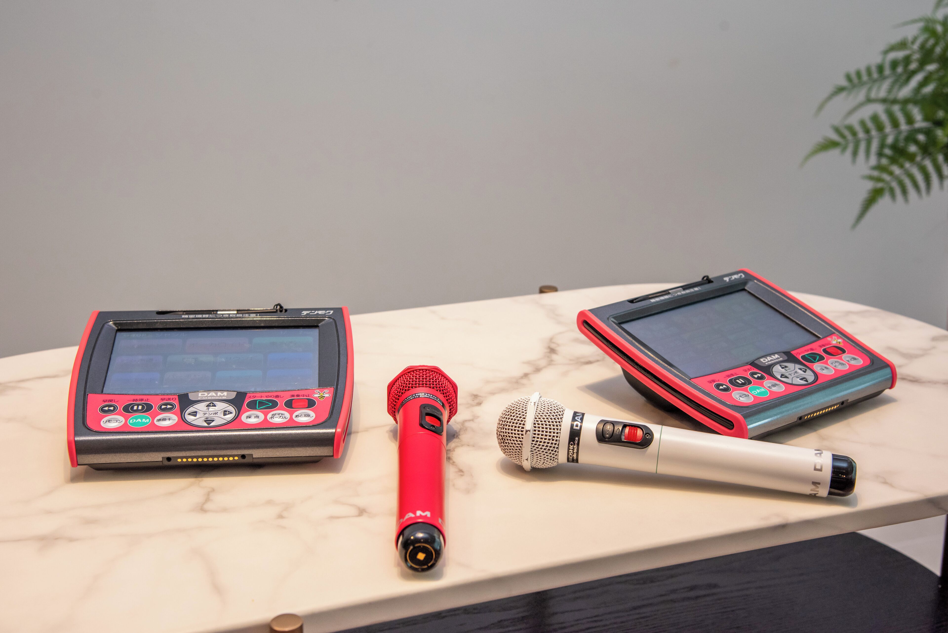 Deux appareils électroniques sur une surface en marbre, un microphone et un petit objet rouge.