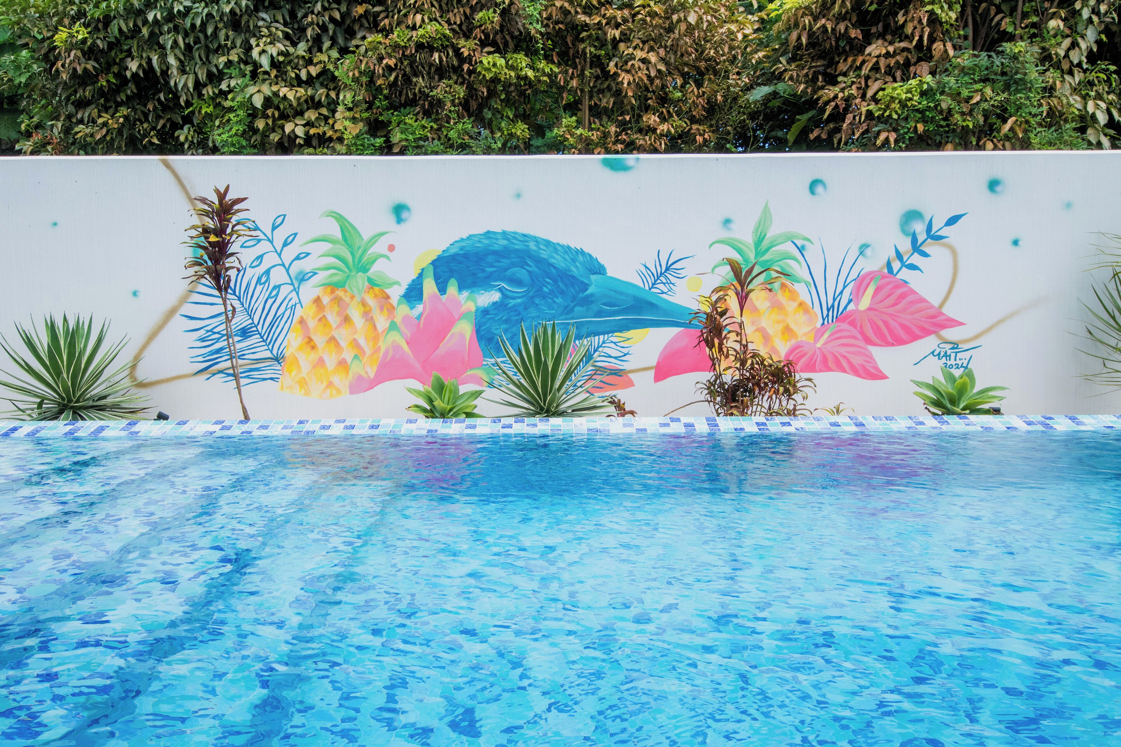 Una piscina con un mural de plantas tropicales y un ave.