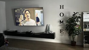 A living room with a flat-screen TV mounted on the wall, a black entertainment unit below it, and a potted plant to the right. - Cozy Whitby Retreat (Private 2 Bedroom Townhouse) (Whitby)