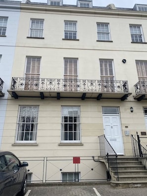 A multi-story building with a balcony featuring ornate metal railings and a white door.