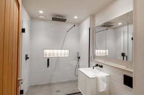 A modern bathroom with a glass shower enclosure, a white sink with a towel, and a large mirror.