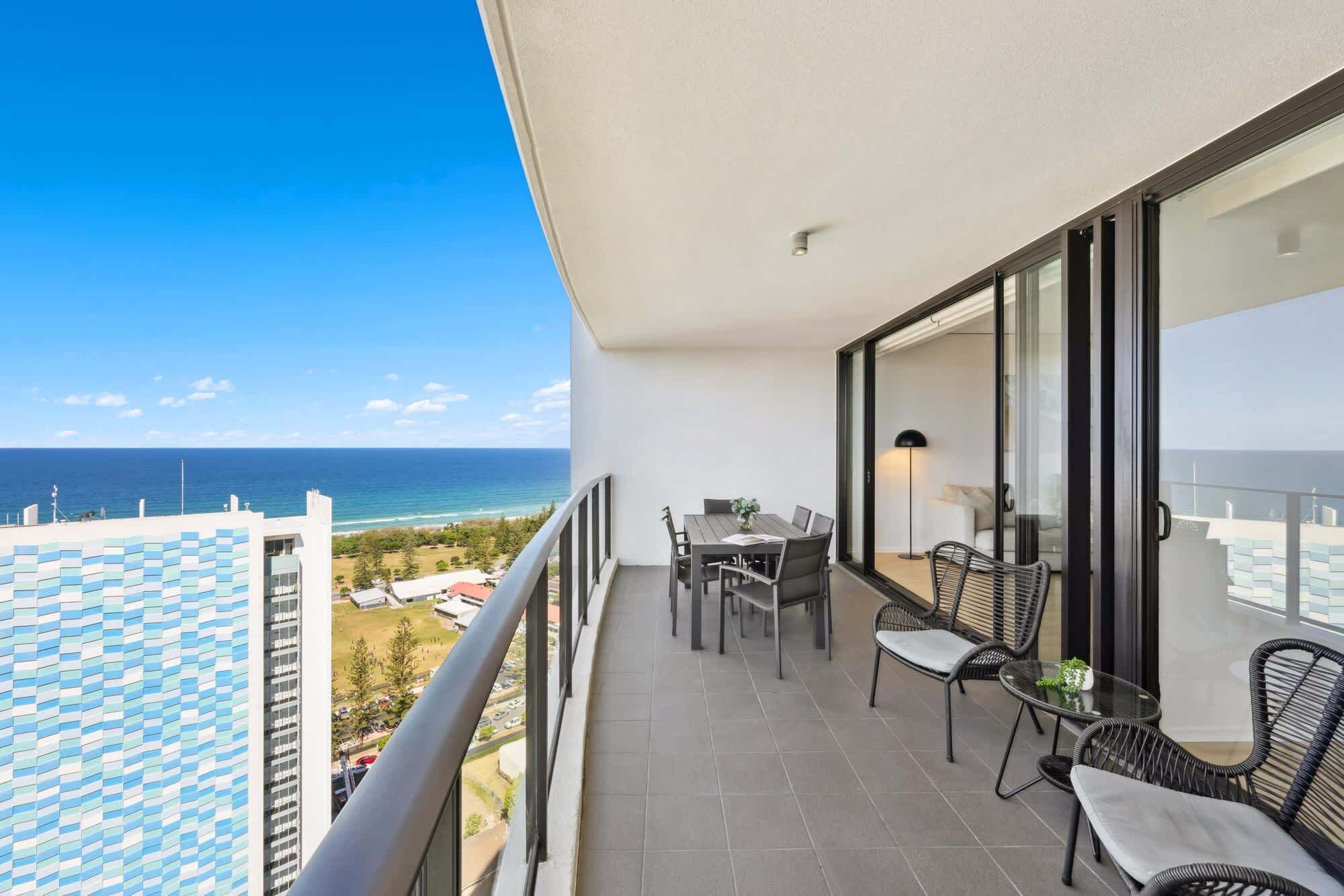 A balcony with a table and chairs, a view of the ocean, and a patterned floor.